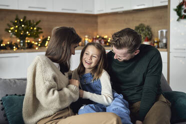 Lächelndes Mädchen mit Eltern auf dem Sofa im Wohnzimmer sitzend - ABIF01725