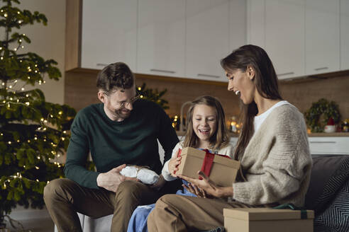 Happy parents giving Christmas gift to daughter sitting on sofa - ABIF01726