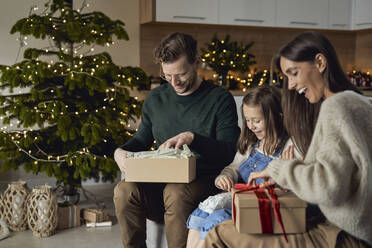Happy parents with daughter opening Christmas present in living room - ABIF01729