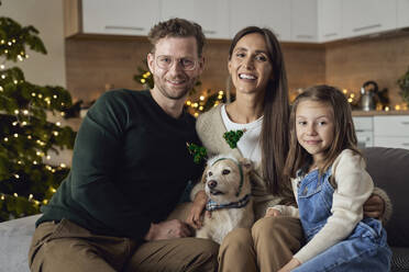 Lächelnde Familie mit Hund auf dem Sofa im Wohnzimmer sitzend - ABIF01736