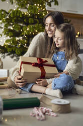 Smiling mother embracing daughter with Christmas gift at home - ABIF01740