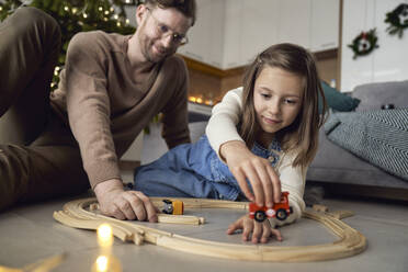 Lächelnder Mann und Tochter spielen mit Miniatur-Eisenbahn zu Hause - ABIF01747