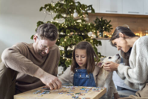 Smiling man and daughter joining puzzle by woman with dog at home - ABIF01748