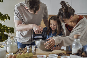 Lächelnde Familie beim Mischen von Keksteig in der Küche - ABIF01754