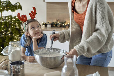 Mädchen sieht Mutter an, die in der Küche Keksteig mischt - ABIF01764