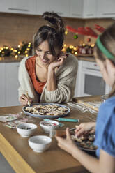 Lächelnde Mutter mit Tochter beim Verzieren von Lebkuchen in der Küche - ABIF01780