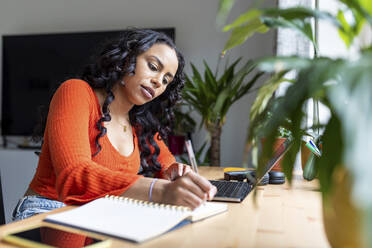 Young freelancer writing in notebook at desk - WPEF05987