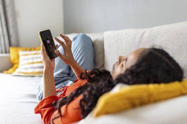 Young woman switching off smart phone lying on sofa at home - WPEF06006