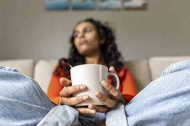 Thoughtful woman with coffee cup sitting in living room - WPEF06019