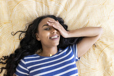 Smiling woman covering eye with hand lying on bed at home - WPEF06040