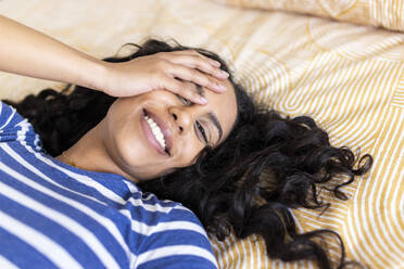 Happy woman covering eye with hand lying on bed at home - WPEF06042