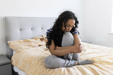 Young woman hugging knee on bed in bedroom - WPEF06043