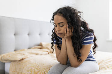 Sad woman with hand on chin in bedroom - WPEF06046