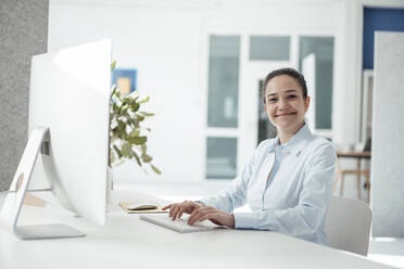 Glückliche Geschäftsfrau mit Computer auf dem Schreibtisch im Büro - JOSEF10536