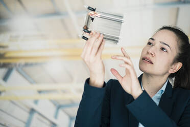 Businesswoman analyzing machine part in factory - JOSEF10553