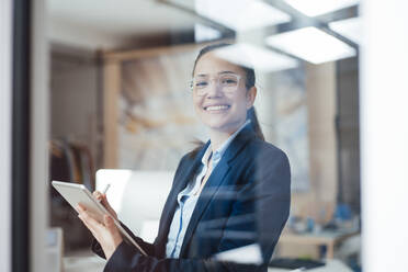 Glückliche Geschäftsfrau mit Tablet-PC, gesehen durch das Glas des Büros - JOSEF10562