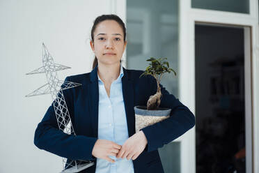 Businesswoman with electricity pylon model and potted plant at office - JOSEF10564