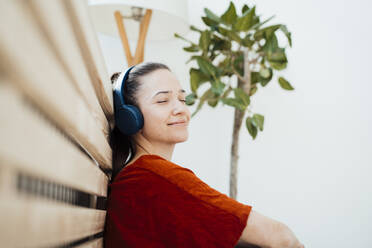 Lächelnde Frau ruht sich mit Kopfhörern zu Hause aus - JOSEF10573