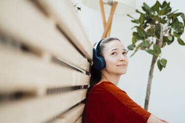 Thoughtful woman listening music through headphones at home - JOSEF10574