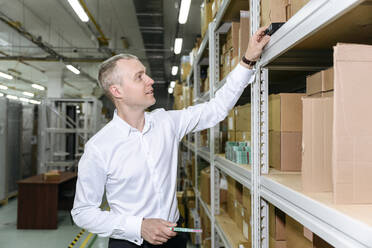 Businessman analyzing machine part on rack at factory - EYAF01945