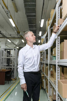 Businessman examining machine part on rack in factory - EYAF01946