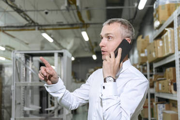 Geschäftsmann, der in einer Fabrik mit einem Mobiltelefon spricht - EYAF01949