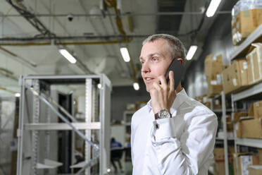 Geschäftsmann, der in einer Fabrik mit einem Smartphone telefoniert - EYAF01950