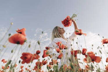 Lächelnde Frau, die an einer Blume im Feld riecht - SIF00176