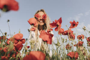 Glückliche Frau, die ihre Augen mit einer Blume im Mohnfeld bedeckt - SIF00178