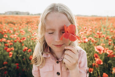 Girl covering eye with red flower in field - SIF00184