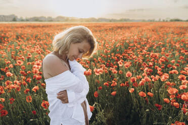Smiling woman hugging self in poppy field on weekend - SIF00193