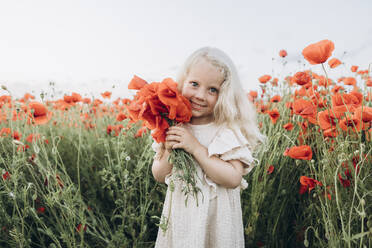 Lächelndes Mädchen hält rote Blume in Mohnfeld - SIF00206