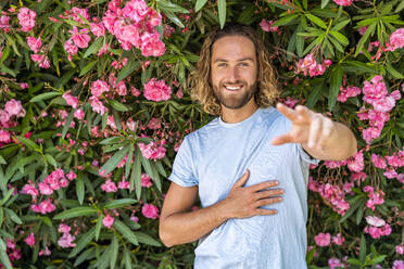 Lächelnder Mann, der vor rosa blühenden Pflanzen gestikuliert - DLTSF02937