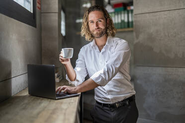 Führungskraft mit Kaffeetasse und Laptop auf einem Tisch im Büro - DLTSF02943