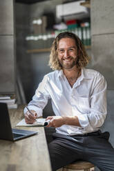 Smiling businessman with pen and diary in office - DLTSF02946