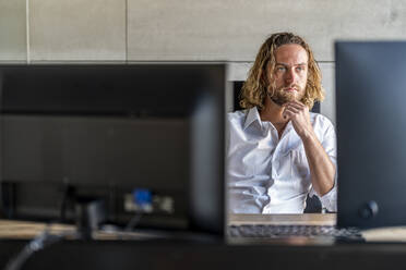 Thoughtful executive sitting with hand on chin at desk in office - DLTSF02949