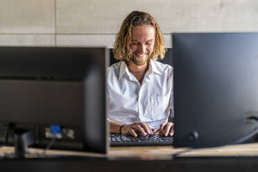 Lächelnde Führungskraft mit Desktop-PC am Schreibtisch im Büro - DLTSF02950
