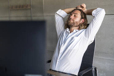 Businessman with eyes closed resting on chair in office - DLTSF02953