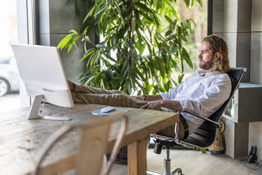 Thoughtful businessman sitting on chair at table in office - DLTSF02955