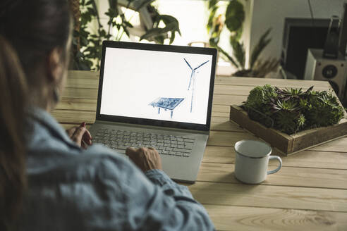 Freiberufler mit Skizze von Solarpanel und Windkraftanlage auf Laptop-Bildschirm im Home-Office - UUF26489