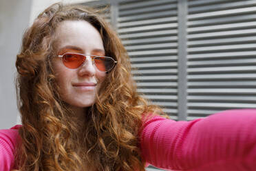 Smiling redhead woman with sunglasses taking selfie - TYF00263