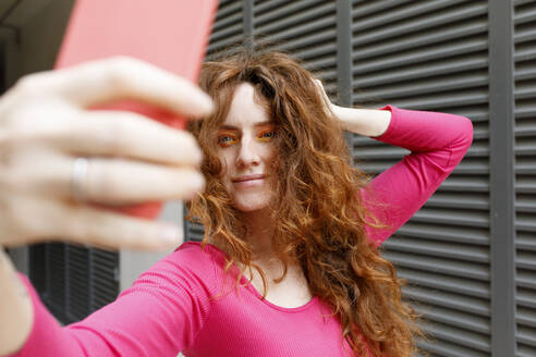 Lächelnde Frau mit Hand im Haar, die ein Selfie mit ihrem Smartphone macht - TYF00267