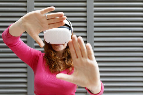 Frau mit Virtual-Reality-Simulator gestikuliert vor einer Wand - TYF00271