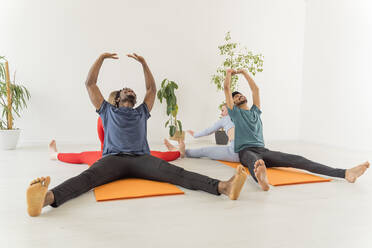 Multiracial couples practicing stretching exercise together in yoga studio - OSF00113