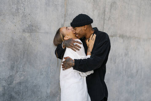 Fröhliches junges Paar umarmt sich vor einer Mauer - MMPF00156