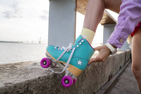 Woman adjusting roller skates standing by railing - VPIF06594