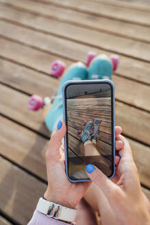 Hände einer Frau, die mit ihrem Smartphone Rollschuhe fotografiert - VPIF06596