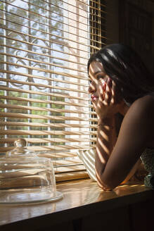 Thoughtful woman looking through window at home - PGCF00111