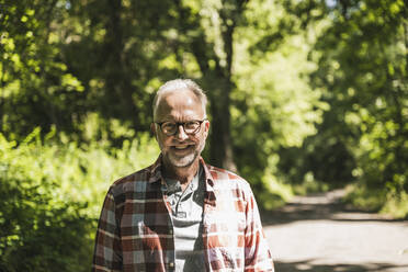 Glücklicher Mann mit Brille steht im Park an einem sonnigen Tag - UUF26517