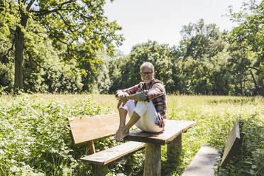 Lächelnder Mann sitzt auf einem Picknicktisch vor Bäumen - UUF26531